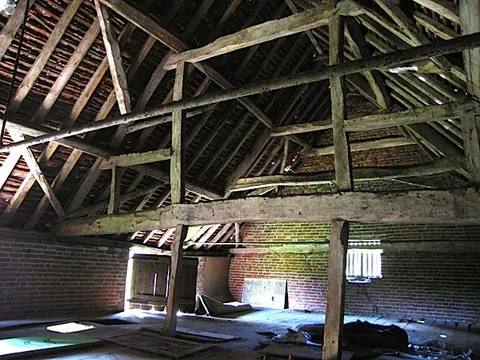 Inside the barn before conversion: bare roof timbers and an earth floor