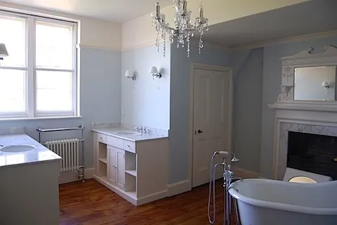 A bathroom with a roll-top bath, fireplace and twin basins on a timber floor