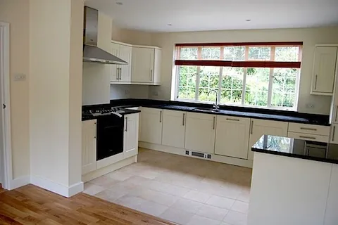 A kitchen with white units, black worktops and a window over the sink