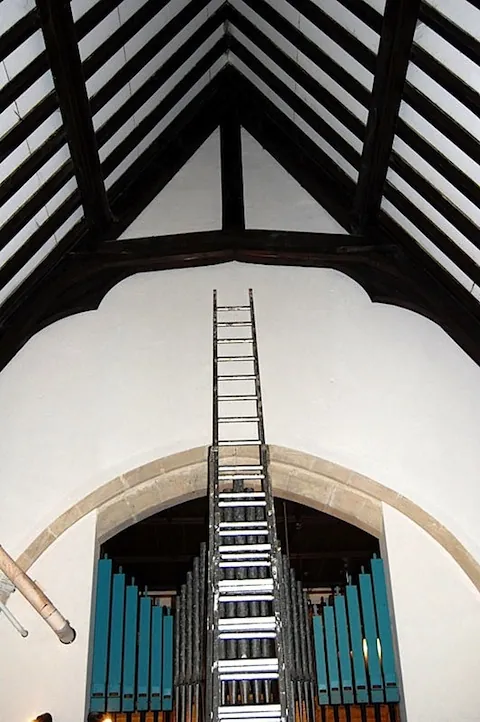 Limewashed walls inside a church, with a ladder rising to the roof timbers