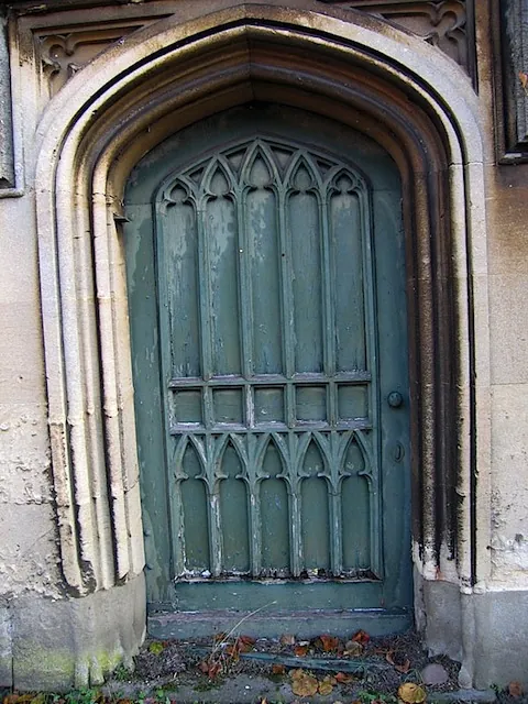 An original carved Gothic door, painted green, in a stone archway