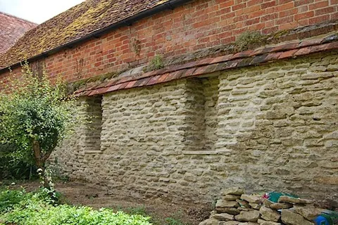A stone wall rebuilt in lime mortar below a brick and tile building